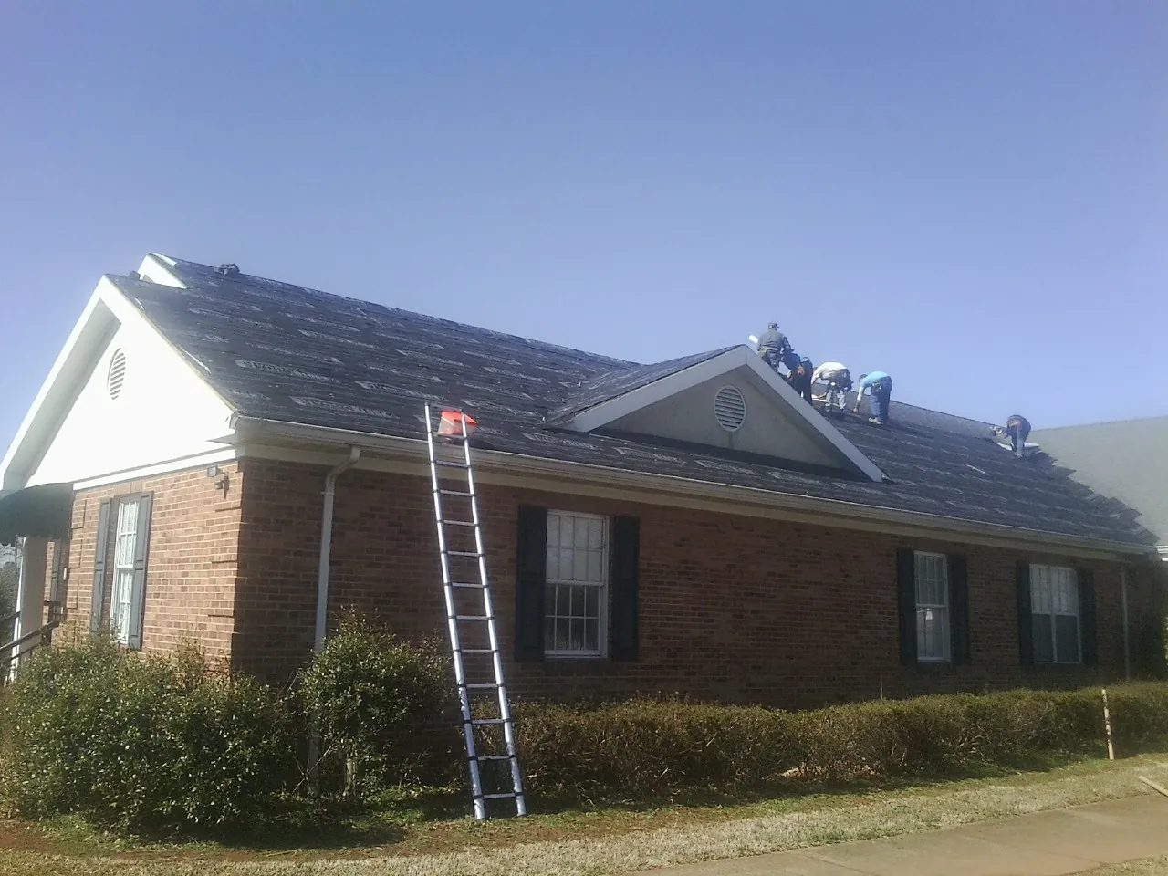 Crew tearing shingles off a brick ranch roof with a ladder set — Emergency Roof Repair work by our crew in Wasco