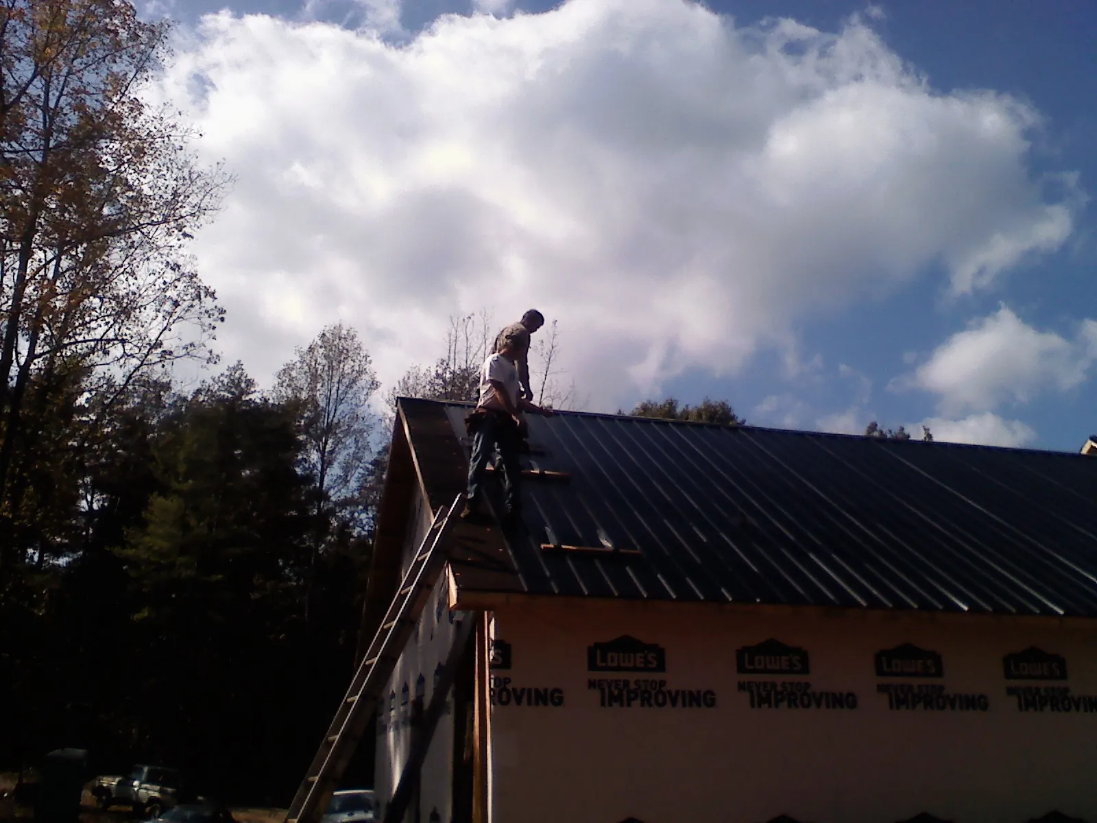 Roofer fastening dark metal panels high against a cloudy sky, from a Roof Inspection job in Wasco