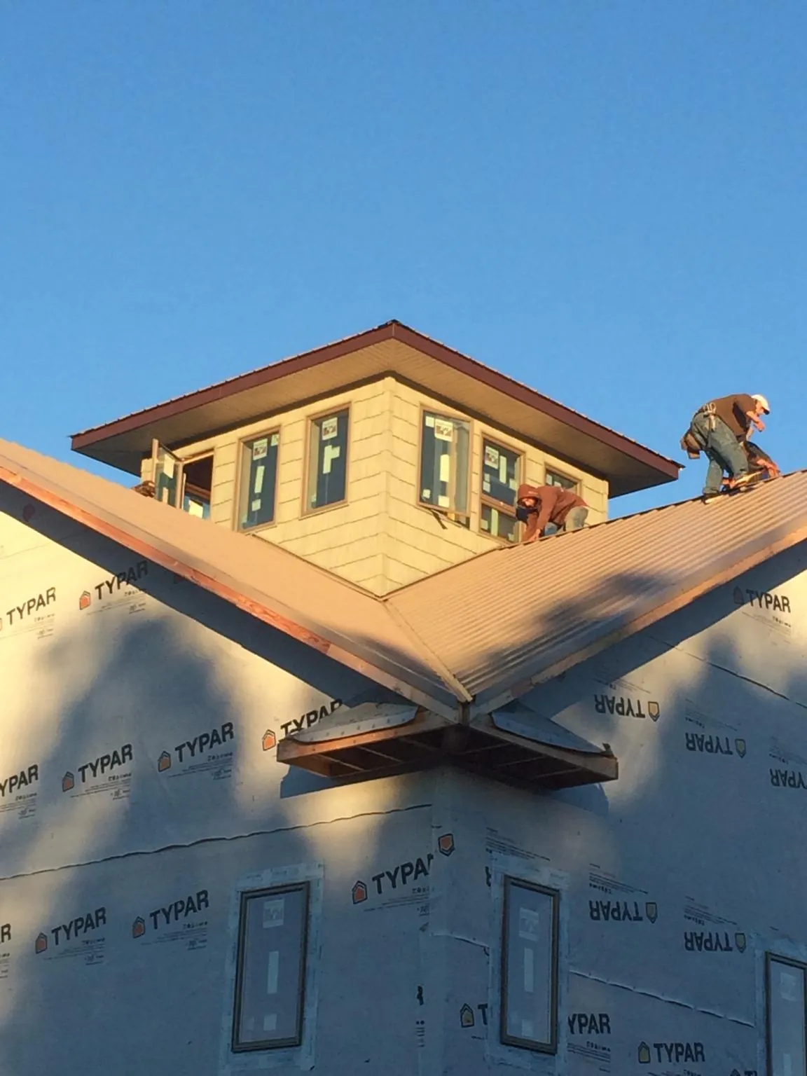 Roofers working around a rooftop cupola on a new metal roof at sunset in Wasco